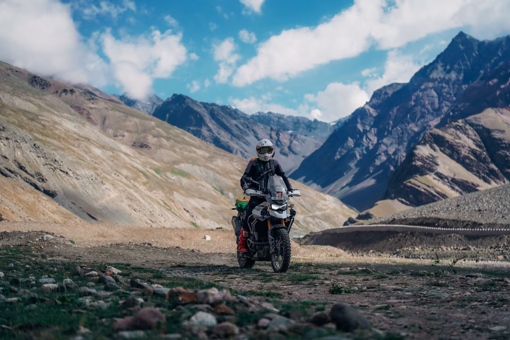 An adventure motorcycle on a dirt road winding through a green Himalayan valley