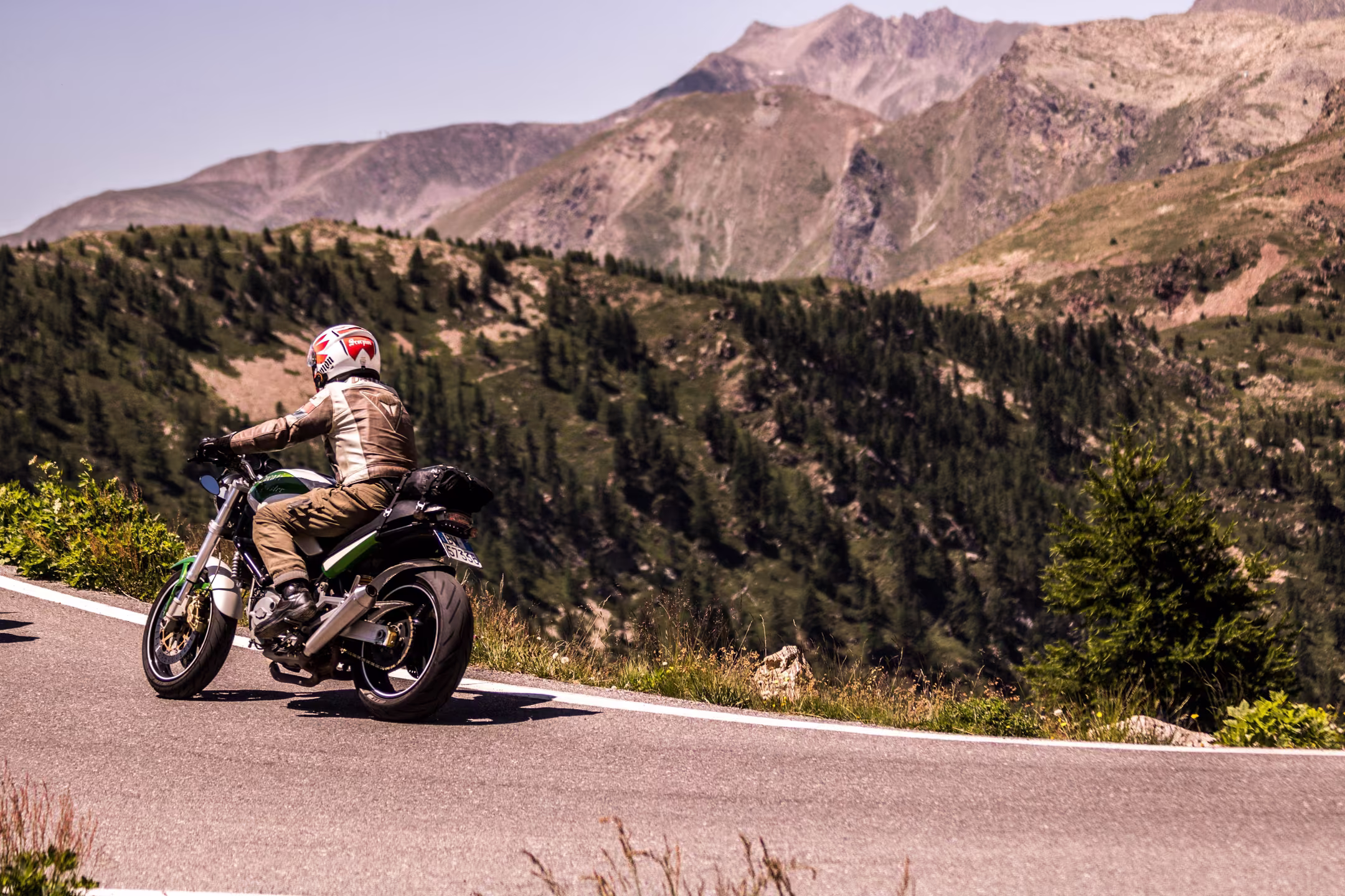 Riding a motorcycle along a paved highway winding through green hills