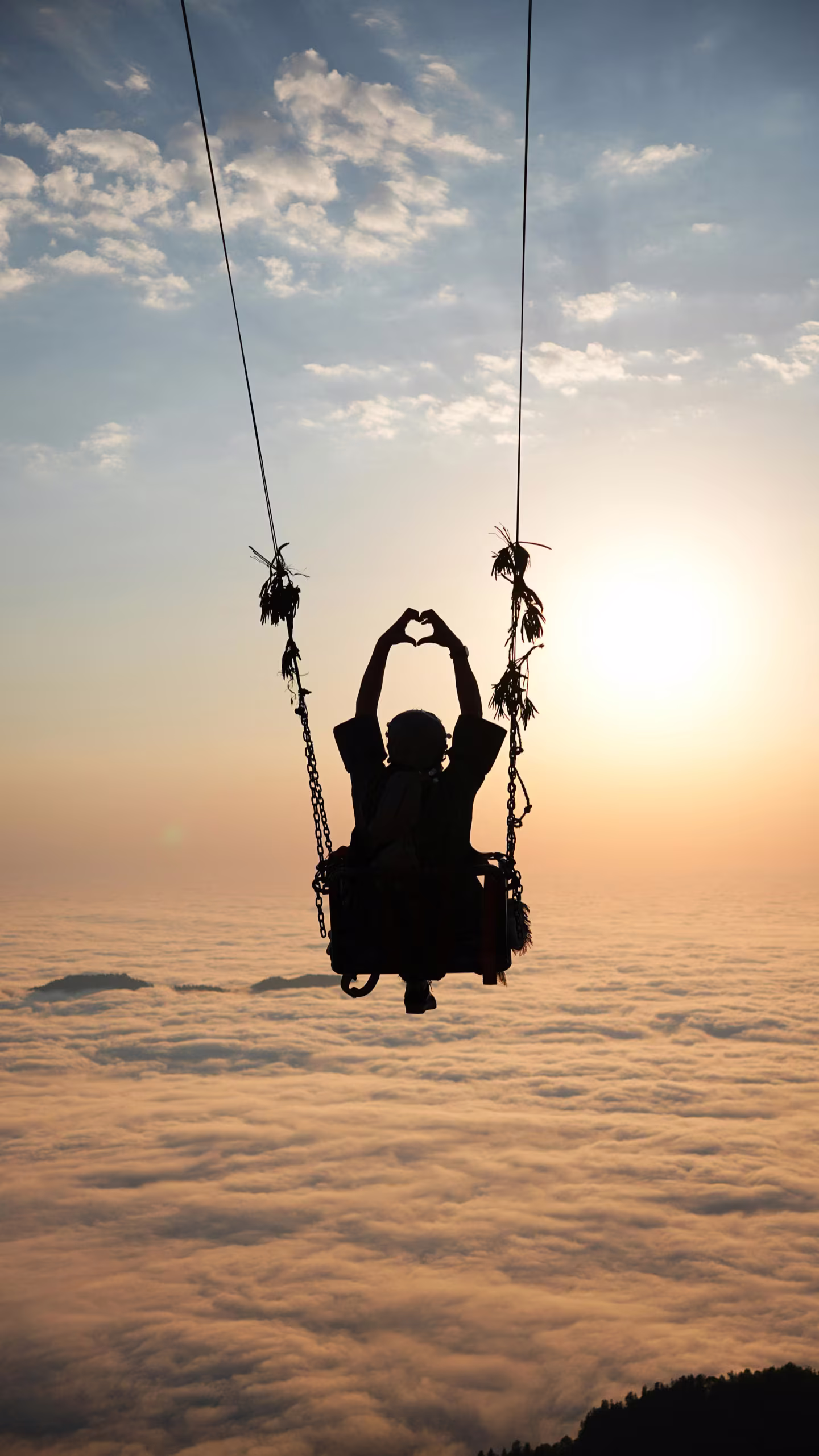 Silhouette of a traveler on a giant swing above the clouds