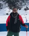 Pratik Poudel in a red trekking jacket and scarf, smiling with a trekking pole on a snowy mountainside