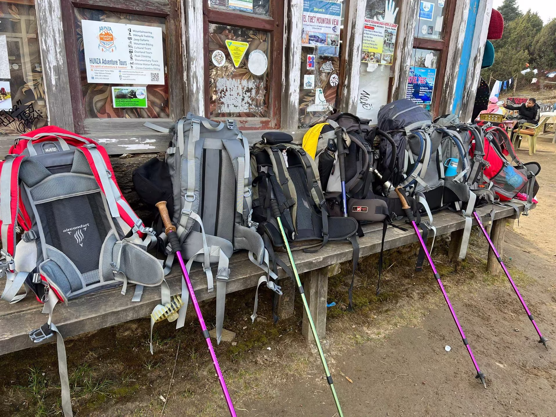 Six trekking backpacks lined up on a bench, ready for departure