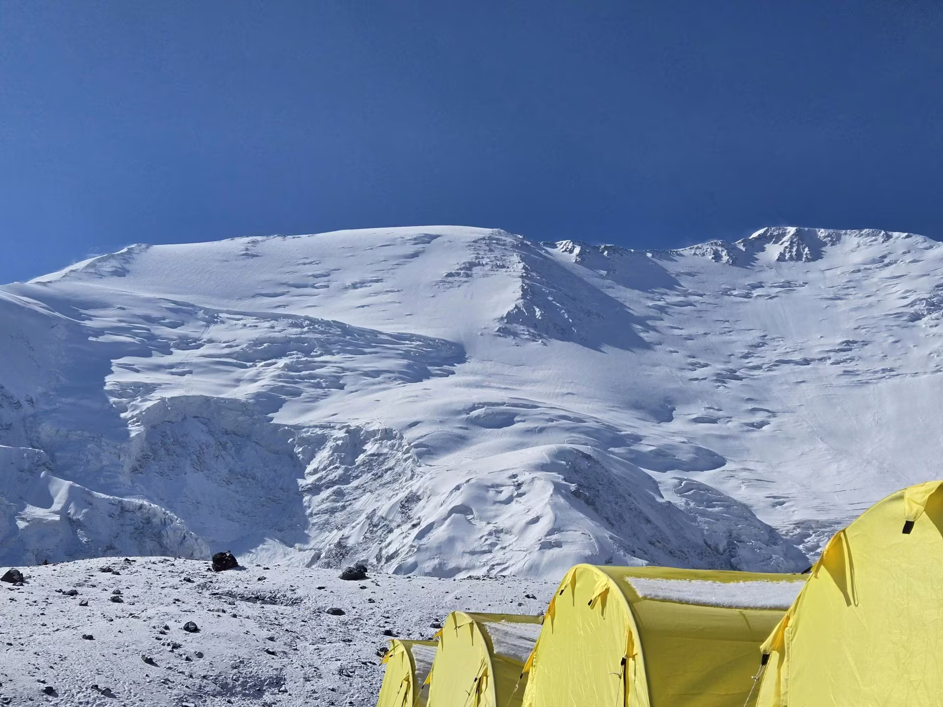 Expedition tents pitched on a high-altitude snow field with a massive Himalayan peak behind