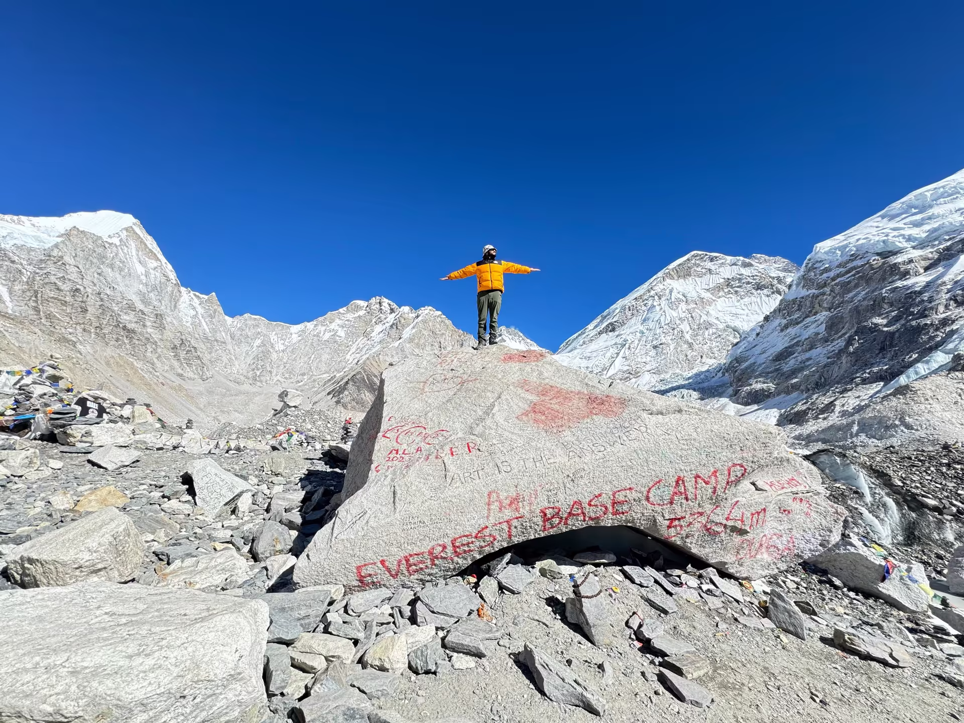 Trekker in yellow jacket standing on the rock marker at Everest Base Camp 5364m