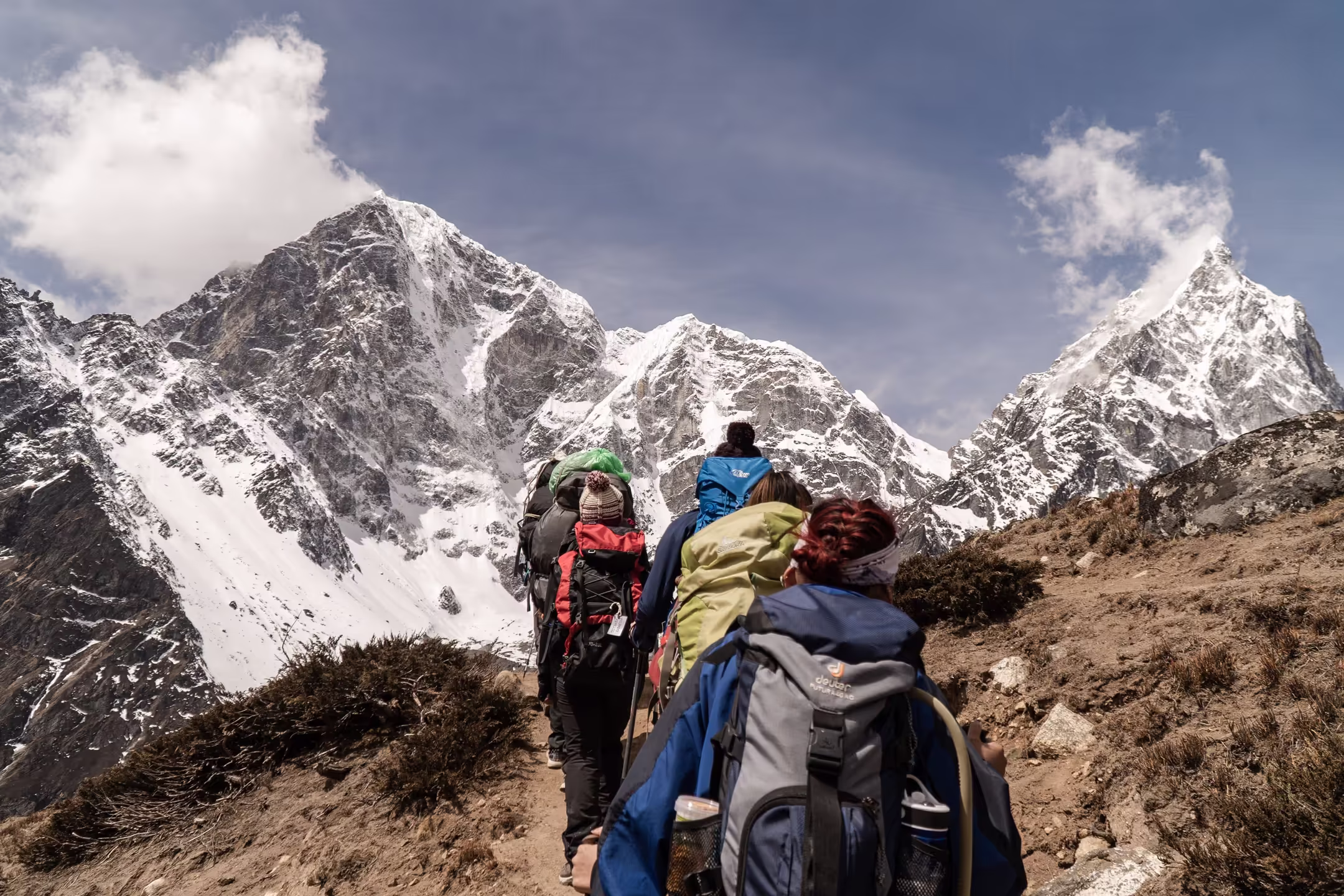 Group of trekkers walking a mountain trail with Himalayan peaks filling the background