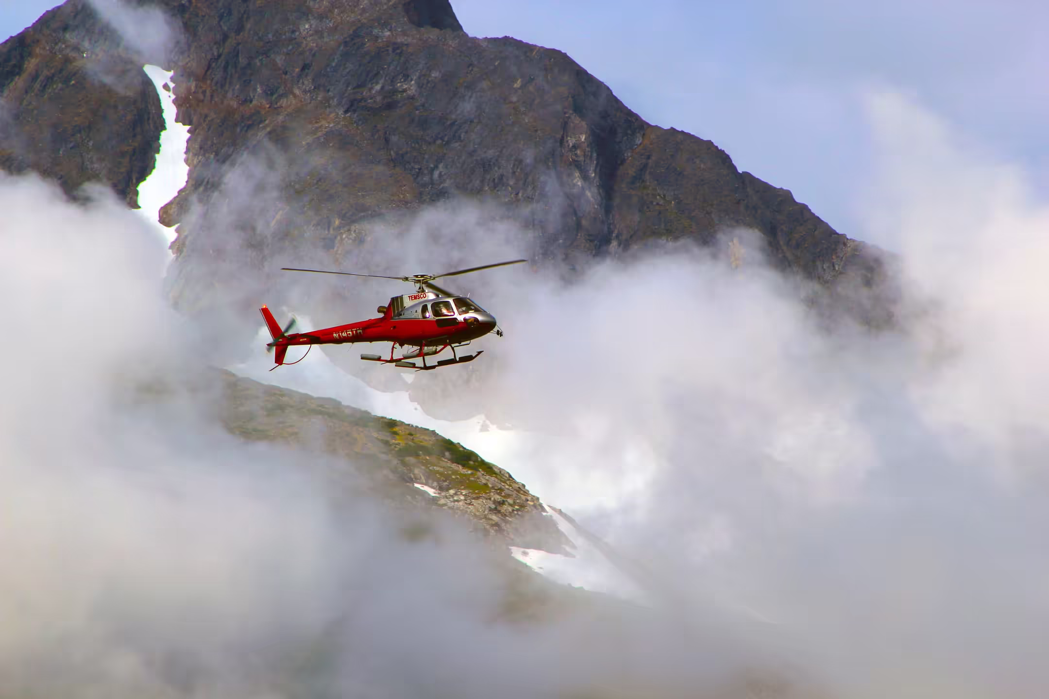 Red rescue helicopter flying through foggy Himalayan hills in Nepal