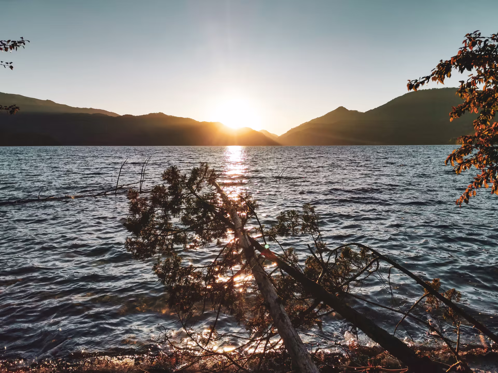 Golden sunset reflected on the still, deep blue surface of Rara Lake surrounded by forested hills