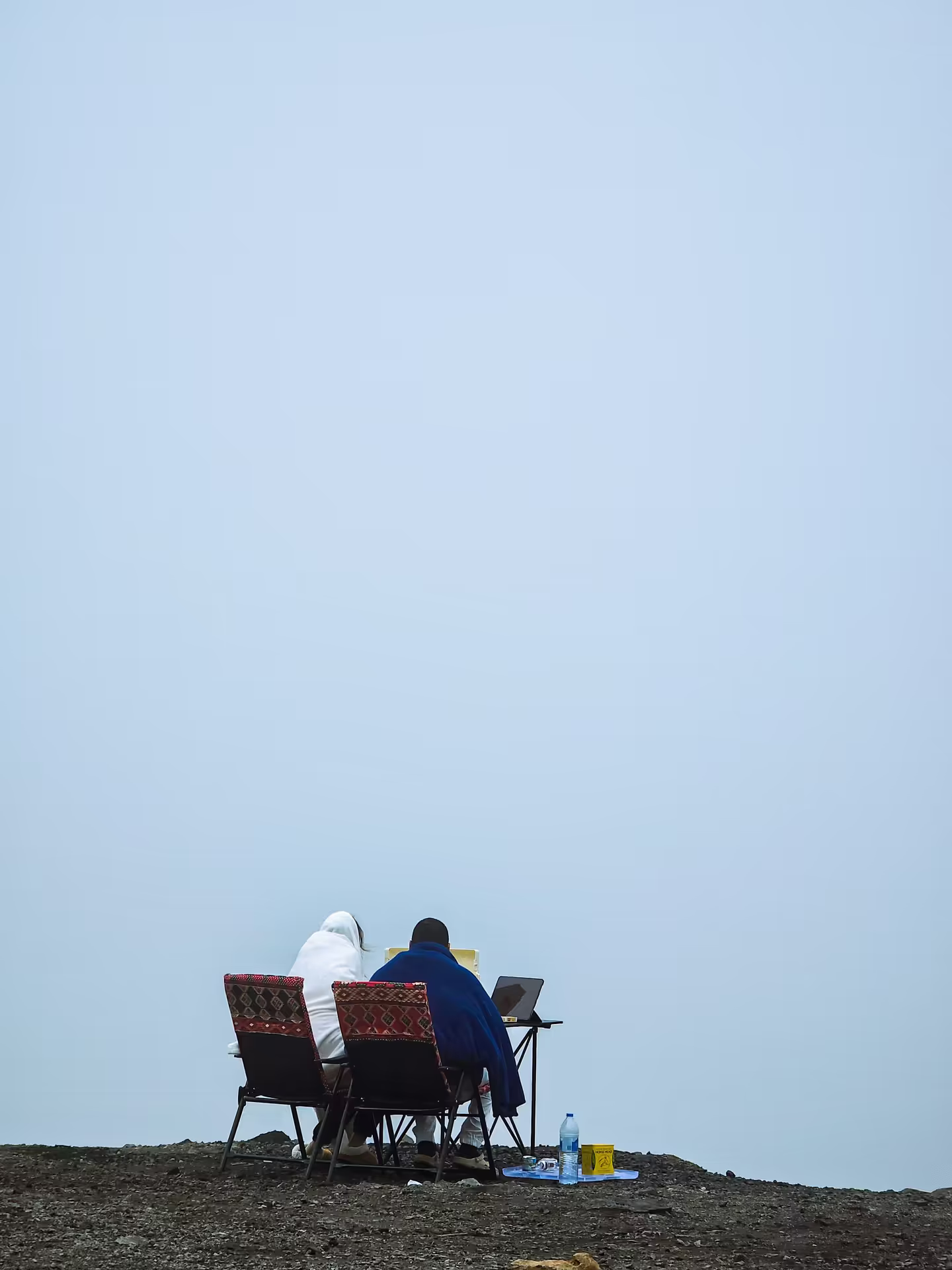 Two people working on laptops from a hilltop with open mountain views